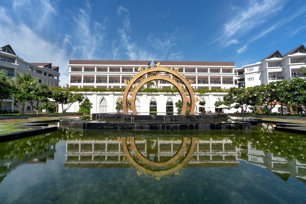 Elegant hotel facade with a stunning fountain reflecting in a serene pool, perfect for relaxation and vacation.