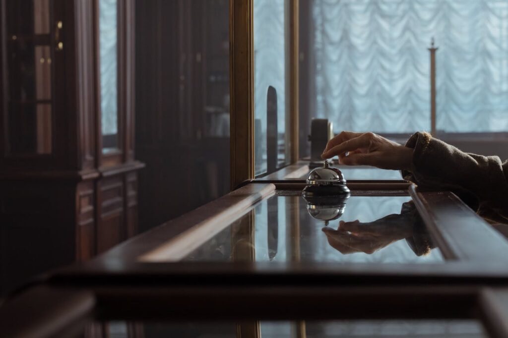 A hand pressing a service bell on an elegant wooden hotel desk, creating a classic atmosphere.